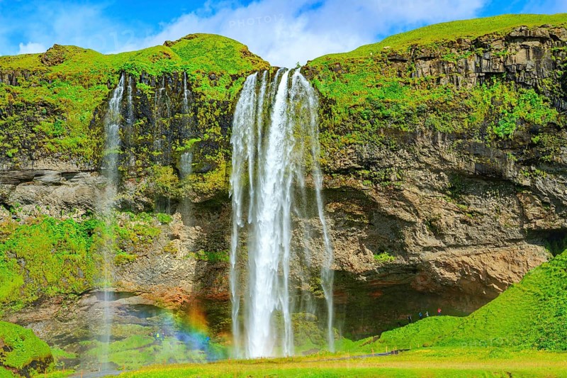 The famous Seljalandsfoss waterfall. Travel to exotic Iceland. Magnificent rainbow appears in the splash of water. Fine July day