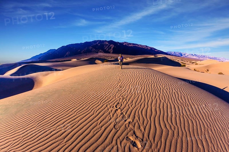 Sunrise in the orange sands of the desert Mesquite Flat, USA. Woman - photographer is among the gently sloping sand dunes