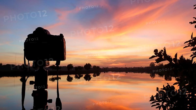 Silhouette of a camera at sunset.Dslr camera shooting on a cityscape sunset with lake reflection