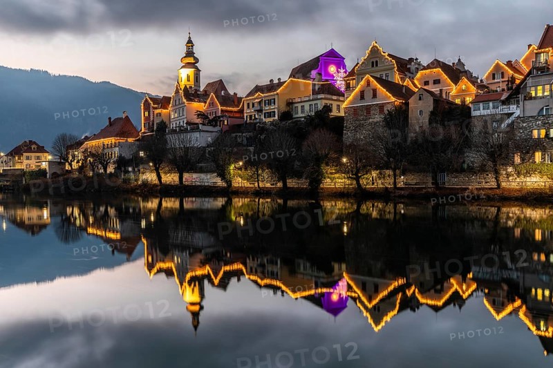 Christmas illuminated house facade of Frohnleiten reflected in the river Mur, Frohnleiten, Styria, Austria