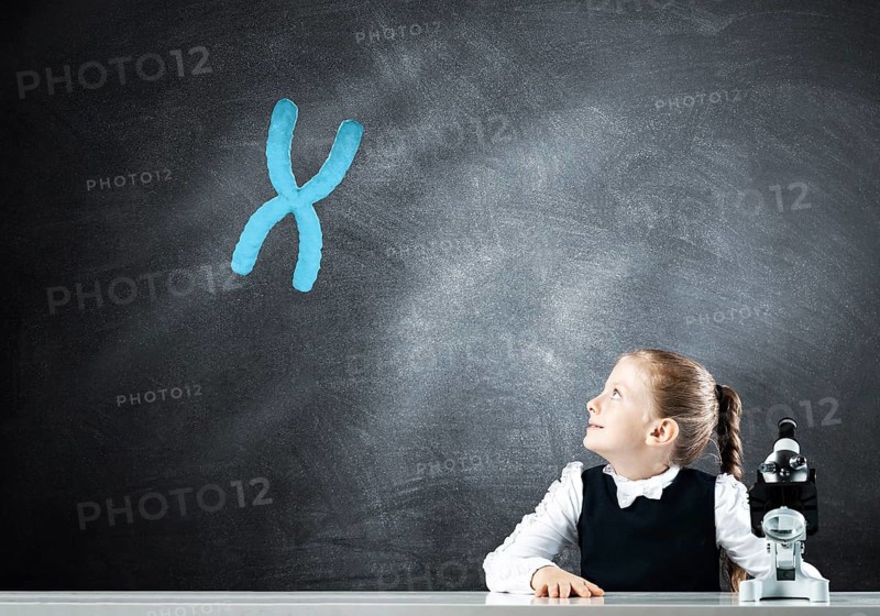 Little girl scientist with microscope on chalkboard background with x chromosome. Research and discovery concept. Elementary science class in modern school. Schoolgirl in schoolwear sitting at desk