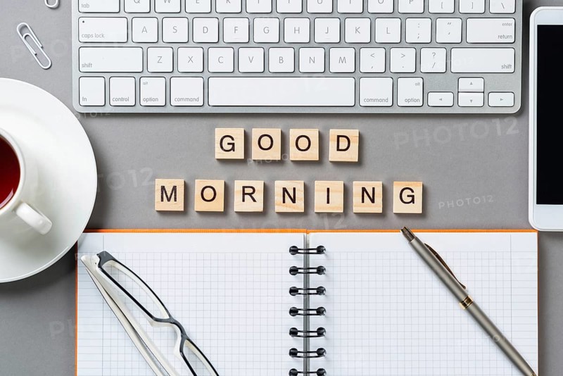 Good morning message with letters on wooden cubes. Still life of workspace with supplies. Flat lay grey surface with computer keyboard and spiral notebook. Morning greeting phrase and motivation