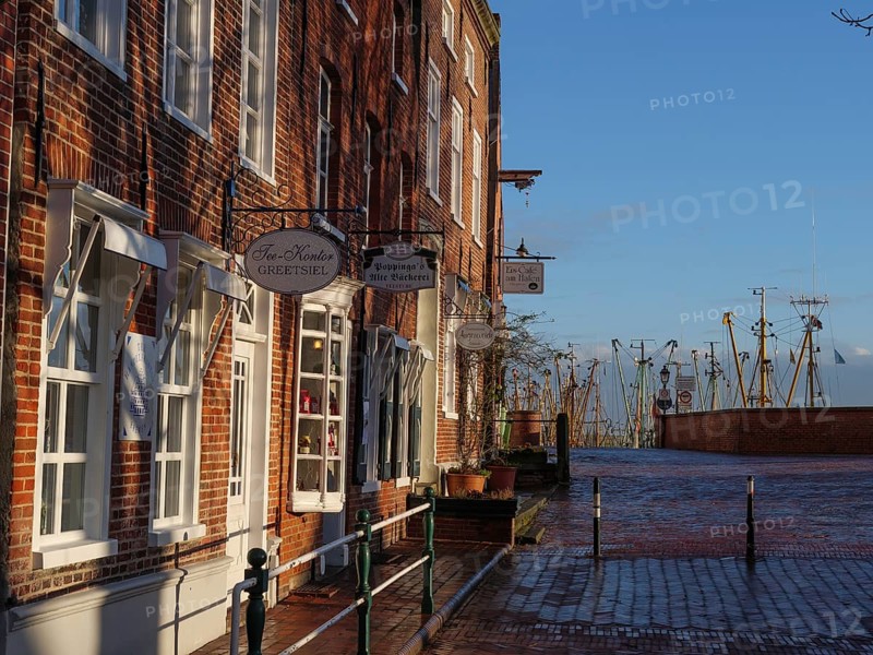 Old town street with traditional buildings, shops and view of the harbour in the winter sun, Greetsiel, East Frisia, Germany