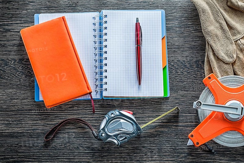 Rolled tape measures safety gloves notebooks pen on wooden board