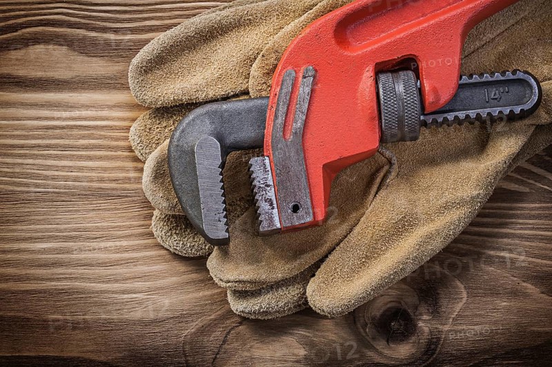 Pair of leather protective gloves pipe wrench on wooden board construction concept