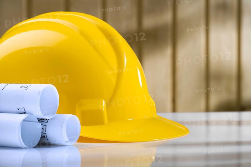 Blueprints and yellow helmet on white table