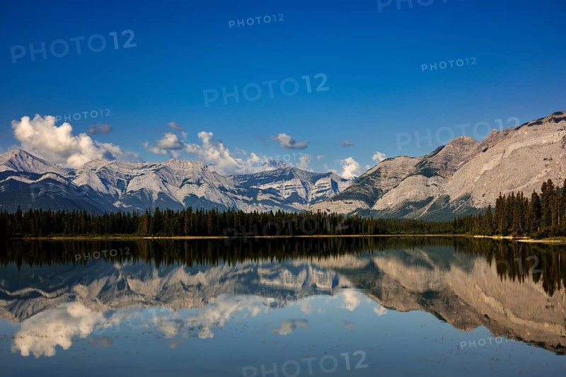 The Canadian Rockies and bright blue sky are reflected in a lake near Canmore, Alberta, Canada, North America