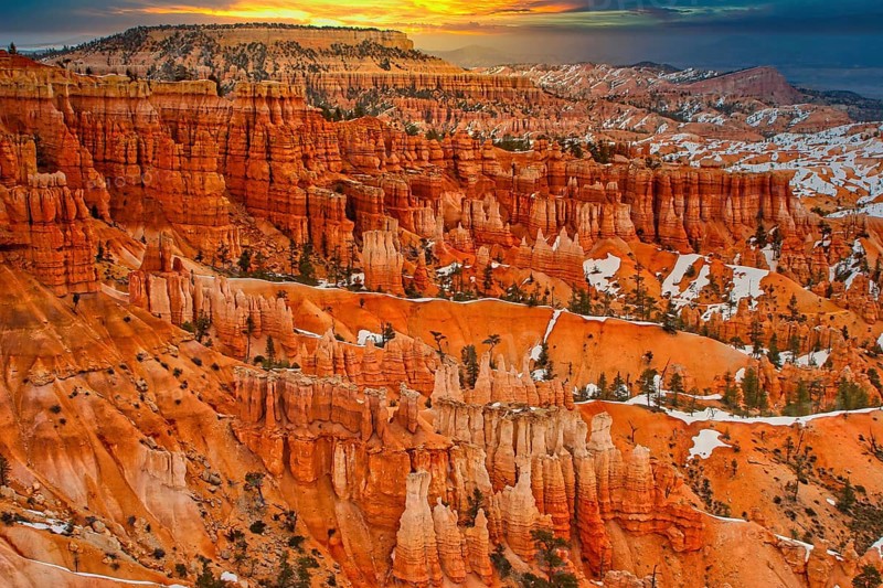 Wide view of a canyon with orange-coloured rocks and snow-covered slopes at sunrise, Bryce Canyon, Utah, America