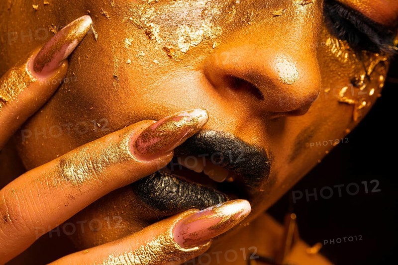 Beauty fashion model girl with golden make up and body on black background. Golden body art. The golden face of a beautiful lady is touching. Artistic portrait