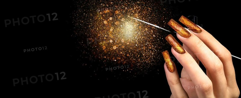 Hand with gold manicure and a brush on a black background covered with sparkles. Nail design. Extended nails