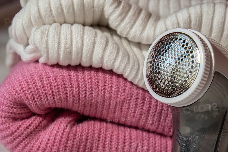 Anti-pilling razor. Device for shaving clothes. Anti-Plush fabric Shaver. Electric portable sweater pill defuzzer Lint remover from pink acrylic or wool sweater. Electric device fabric shaver after cleaning and collected fluff lint. Closeup Pilled sweater. Old used clothes with pilling
