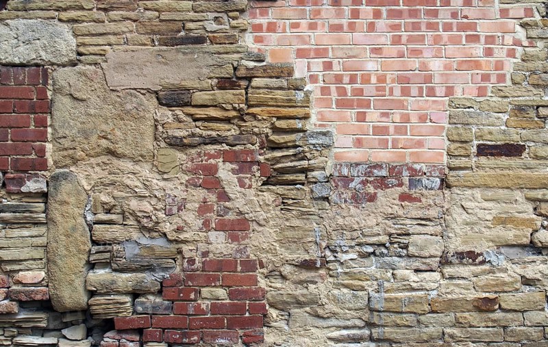A large old wall made of mixed bricks and stone with many jumbled patched and uneven repairs