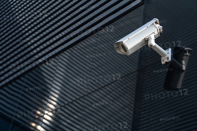 Photo of Modern CCTV camera on a wall. A blurred night cityscape background. Concept of surveillance and monitoring. Toned image double exposure mock up
