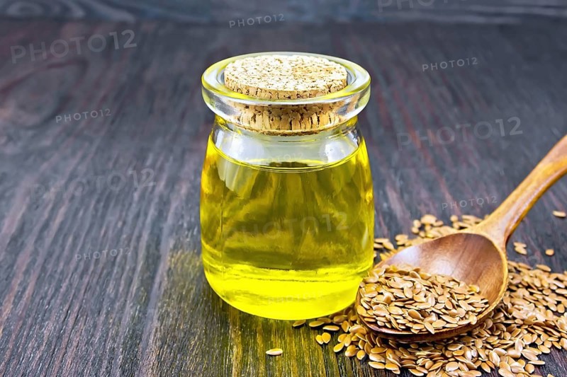 Linseed oil in a glass jar, flax seeds in a spoon against a dark wooden board