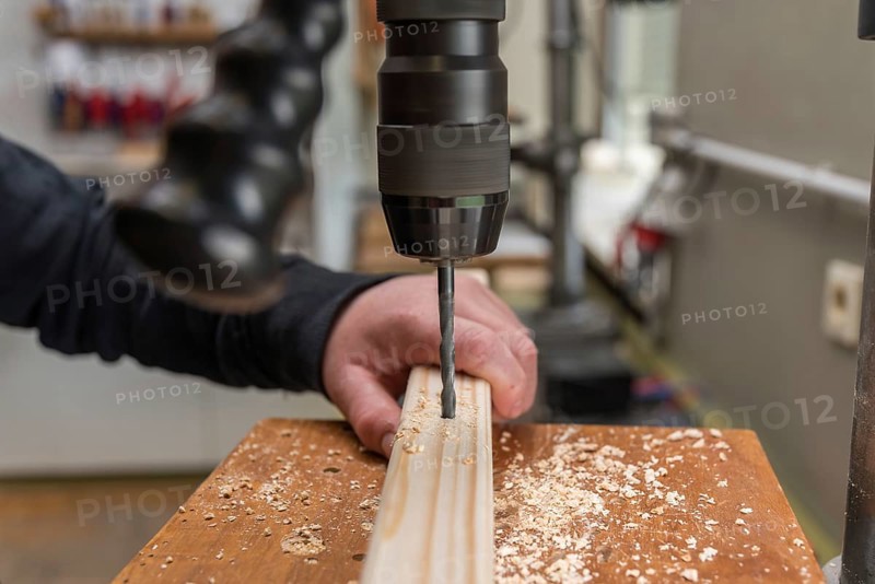 Carpenter drills a hole in the wood with an electric drill - close-up