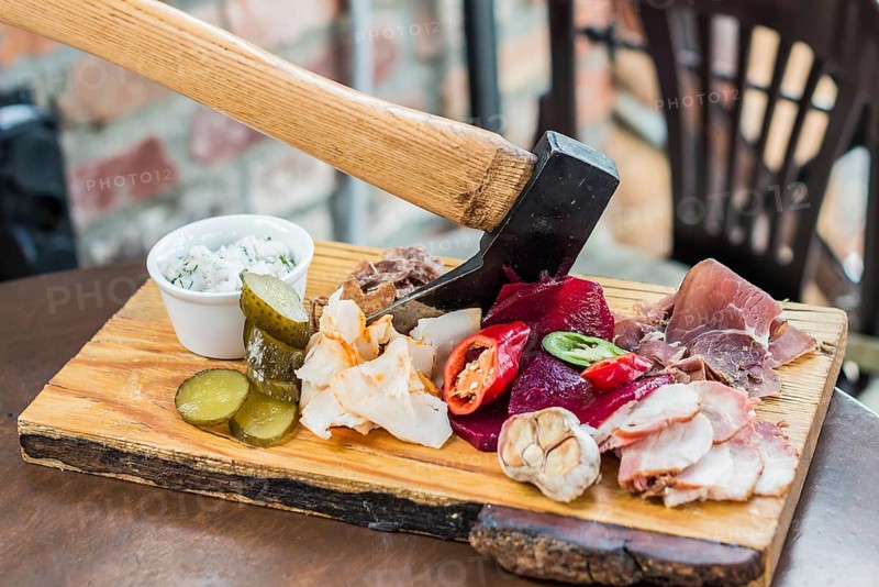 Slices fresh pork meat, lard on wooden board with vegetables, spices, stuck ax on the table