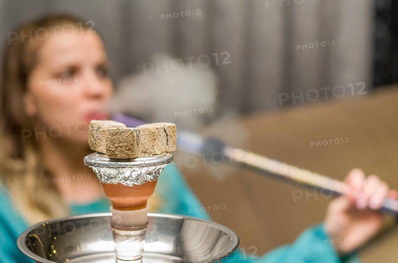Woman in background blurred, smoking traditional Hookah (Narguile, Shisha, Chicha, Arguile), equipment used for smoking tobacco, widely, very widespread throughout the Middle East