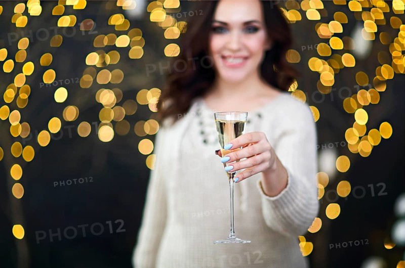 Smiling woman in the sweater with glass of champagne over lights background. Party, drinks, holidays, luxury, friendship and celebration concept