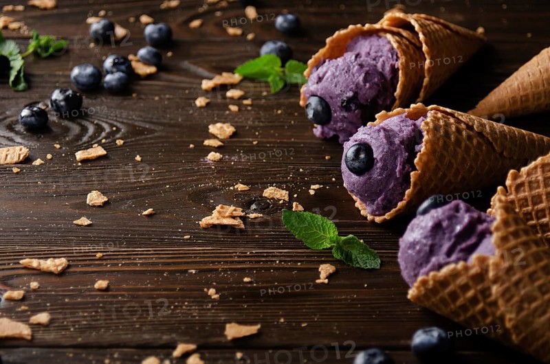 Wafer cones with blackberry icecream on wooden kitchen table with crumbs and berries aside