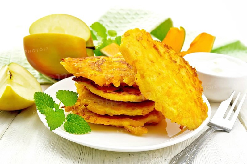 Pumpkin and apple fritters in a white plate, sour cream in a bowl, napkin, mint and fork on wooden board background