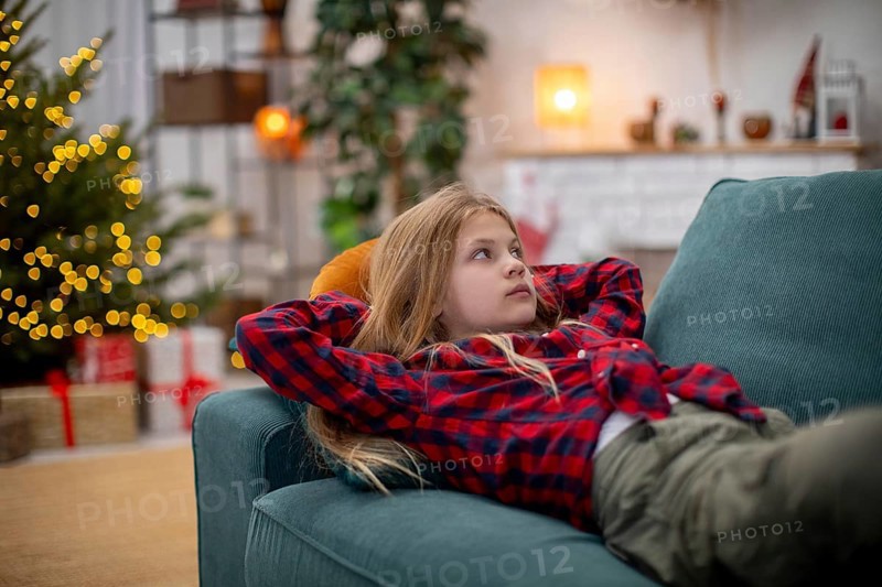 A young child lounges comfortably on a plush sofa, thoroughly enjoying the warm and cozy atmosphere of Christmas