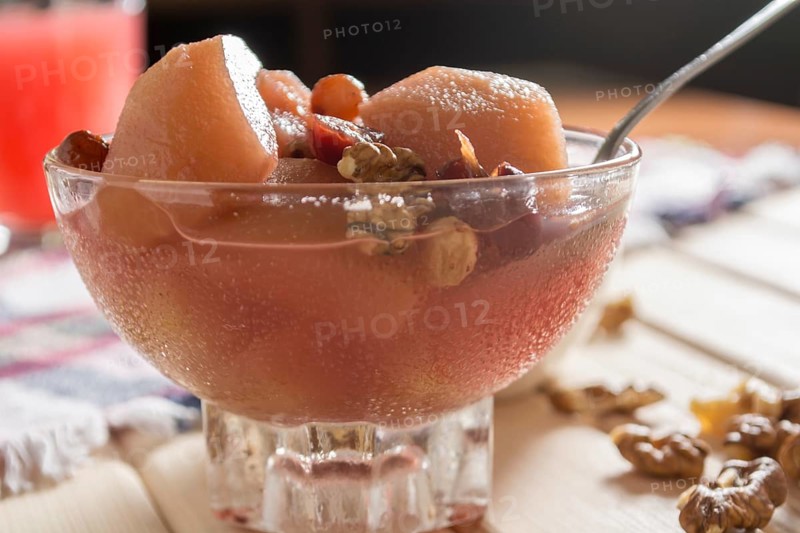 Apple compote with dried fruits in the cup on wooden table with decorative wallnuts
