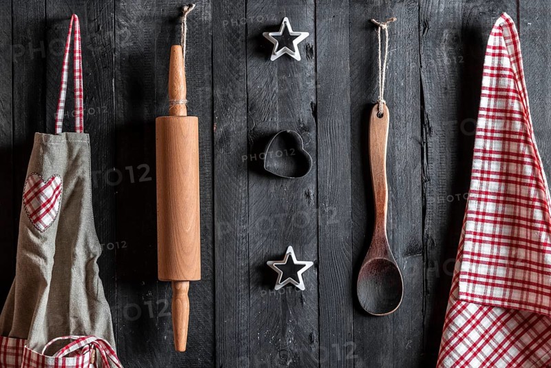 Apron and other kitchen tools hanged with nails on a black wooden wall
