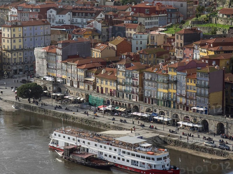 Colourful houses along a riverside street with boats in the river and lively street life, porto, portugal