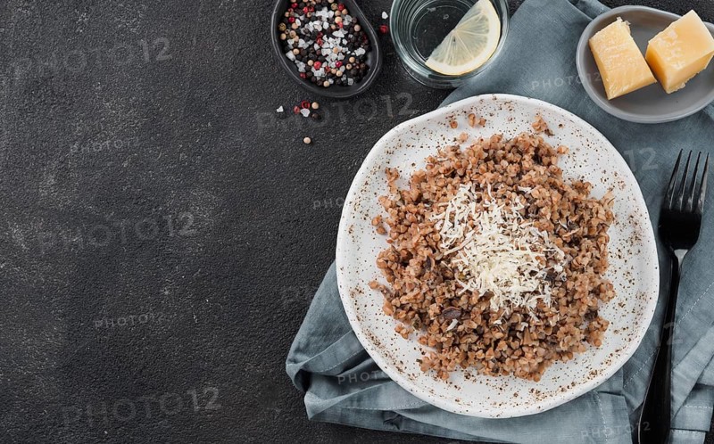 Buckwheat risotto with dried mushrooms served parmesan cheese in craft plate on black cement background. Gluten-free and vegetarian buckwheat recipe ideas. Copy space. Top view or flat-lay