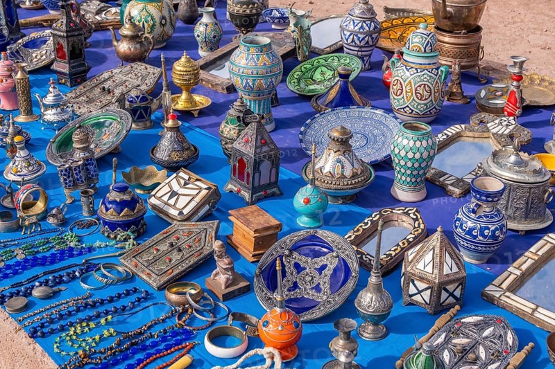 A colorful Moroccan market scene along a bustling street, with vendors selling spices, textiles, and handcrafted goods