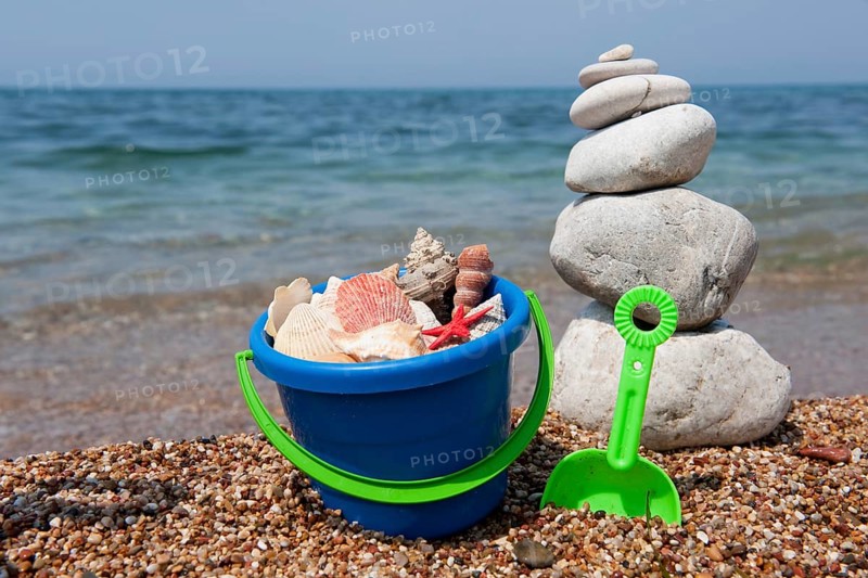 Shells on the beach in colorful bucket with stacked pebbles