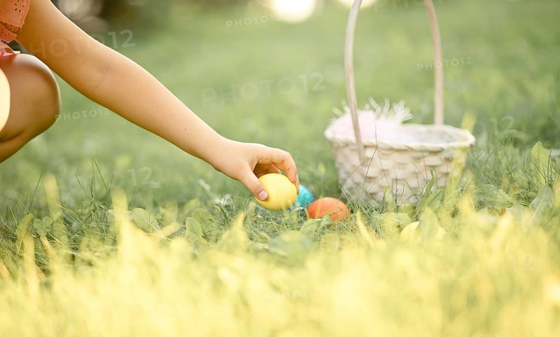 Little cute girl holding basket with colorful painted eggs on Easter egg hunt in park