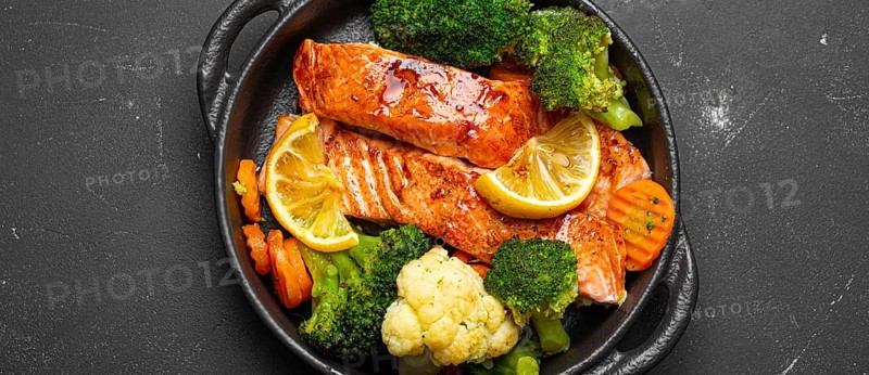 Healthy baked fish salmon steaks, broccoli, cauliflower, carrot in cast iron casserole bowl black dark stone background. Cooking a delicious low carb dinner, healthy nutrition, food photography