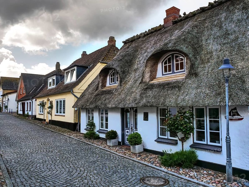 Traditional houses with thatched roofs and cobblestone streets under a cloudy sky, maasholm, germany