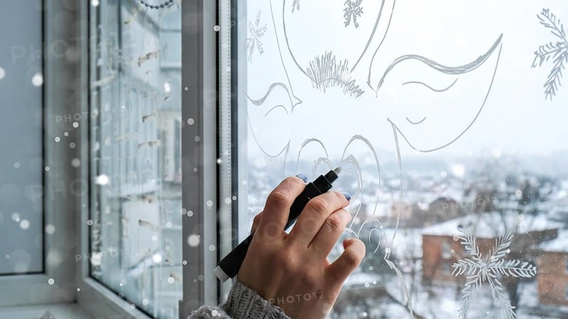 Female hand painting Christmas deer painted on window glass. Christmas winter decor on the window glass. White pattern of deer. Snow art tracery window on holiday season. Diy. Hygge home