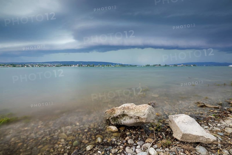 Stormy sky over a calm lakeshore with stones and clear water, Allensbach, Untersee, Lake Constance, Constance District, Baden-Württemberg, Germany