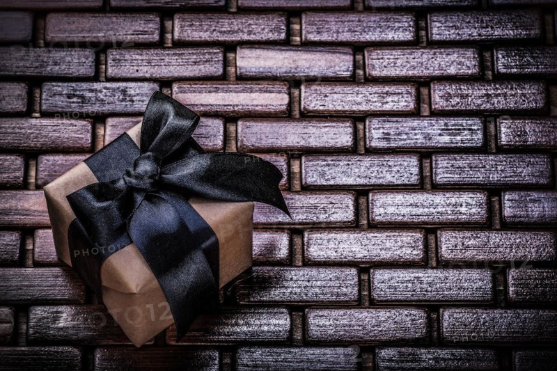 Wrapped present box with black ribbon on wicker wooden mat