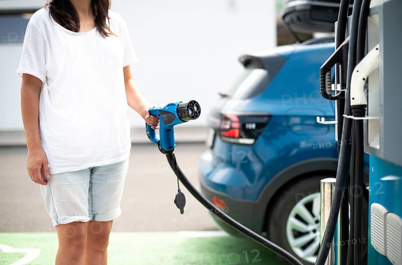 Woman charge her Electric car on gas station. Blue car and electric plug for charging. Ecology fuell concept