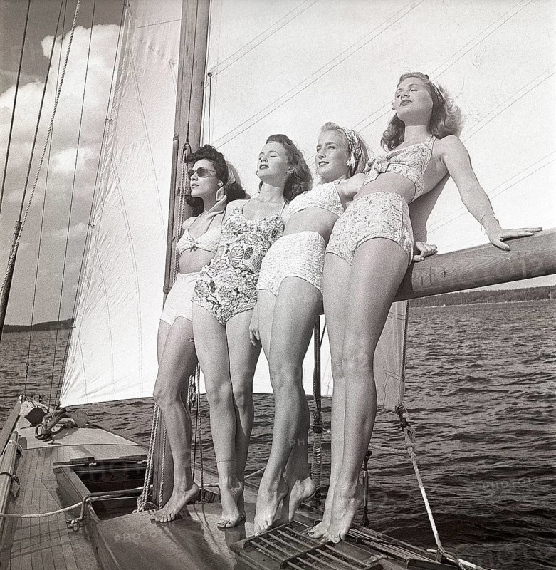 1940s sailing boat. Four young women are standing and leaning against the sails of the boat and enjoys the sunshine and wind. They are wearing the typical 1940s bathingsuit and bikini with high waist. Sweden 1946 Photo Kristoffersson ref AC101-3