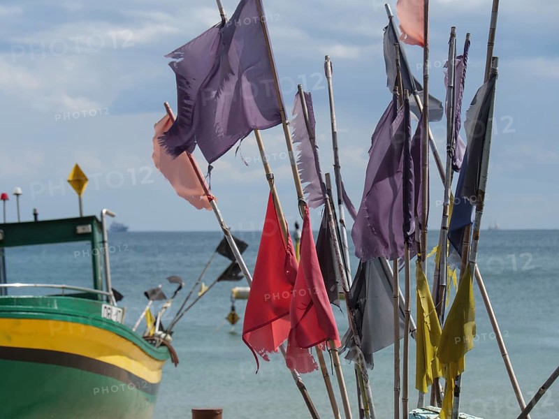 Colourful flags waving in the wind, next to a green boat in front of a wide sea and blue sky, sopot, baltic sea, poland