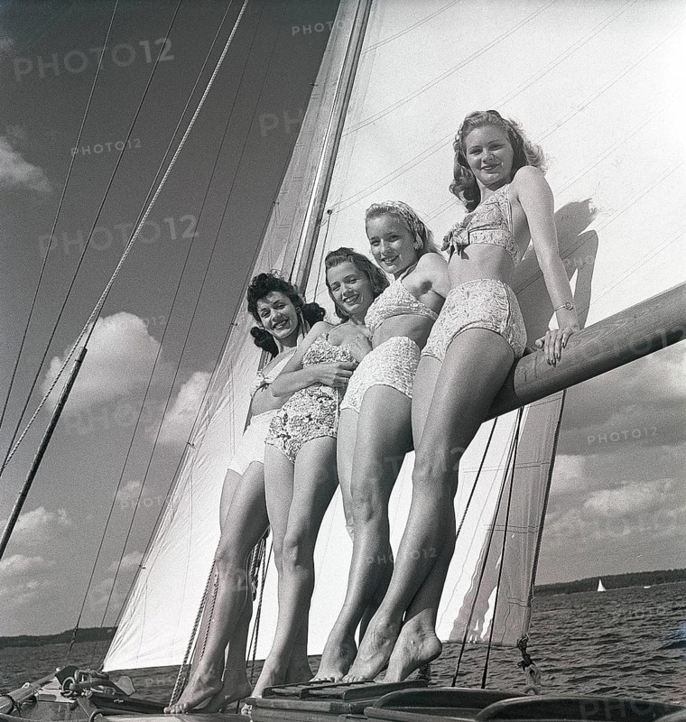 1940s sailing boat. Four young women are standing and leaning against the sails of the boat and enjoys the sunshine and wind. They are wearing the typical 1940s bathingsuit and bikini with high waist. Sweden 1946 Photo Kristoffersson ref AC100-3