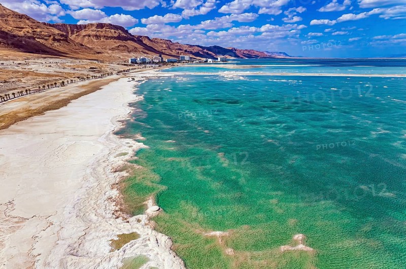 Magnificent Dead Sea. Drone footage. Bright March day. The water reflects the bright blue of the sky. Lush cumulus clouds are reflected in the water. Evaporated salt protrudes from the water