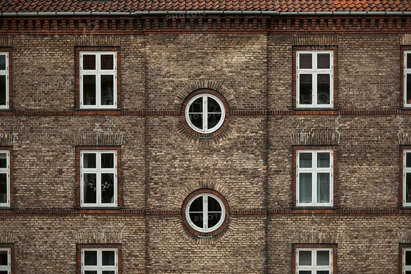 Symmetrical brick building façade with square and round windows, displaying traditional architectural style in Copenhagen, Denmark