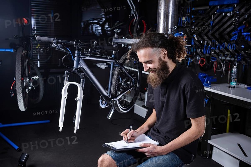 Bicycle Workshop Technician Doing Administrative Work. Bicycle mechanic writing in his checklist notebook. Bicycle mechanic at work. Caucasian worker writing on clipboard in bicycle shop