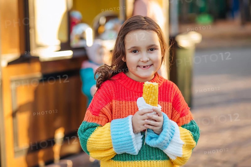 Caucasian little cute girl eating delicious tasty corn on the cob in city park