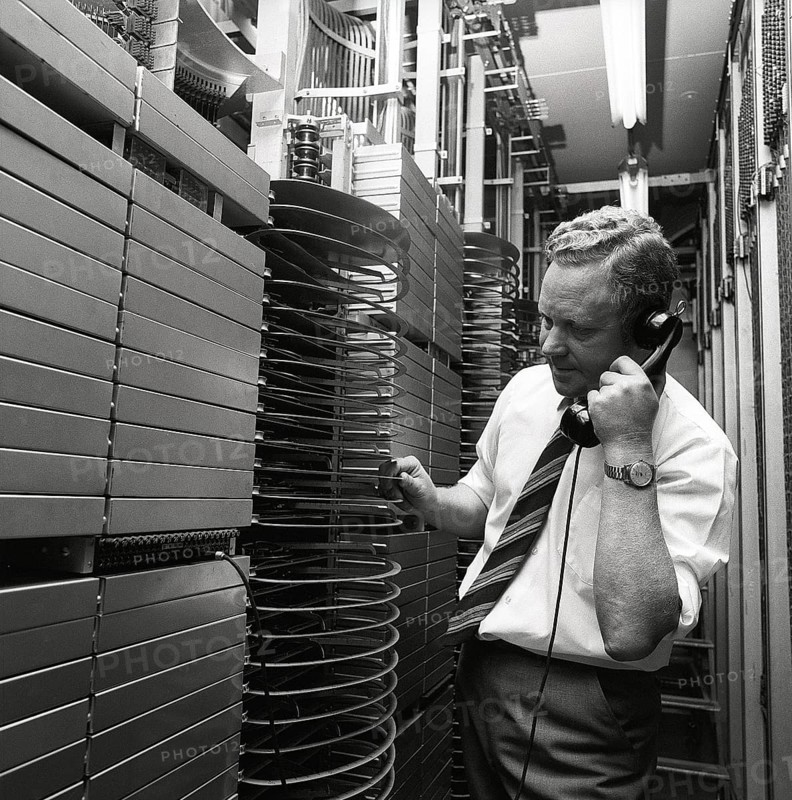 Telephony in the 1970s. A man in a room with an automatic switchboard connecting the calls through a mechanical device that connected the calling and receiving parts. The manufacturer is LM Ericsson. Sweden 1971 Kristoffersson ref ED