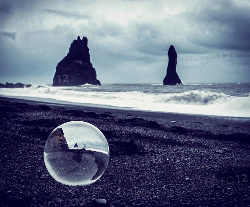 Cold sea water rolling on wet sand near rough stony cliffs on stormy day on Reynisfjara Black Beach in Iceland