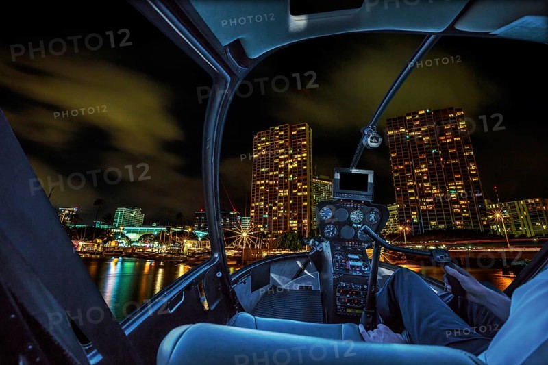 Helicopter cockpit flies in Honolulu skyline by night, Oahu, Hawaii, with pilot arm and control board inside the cabin