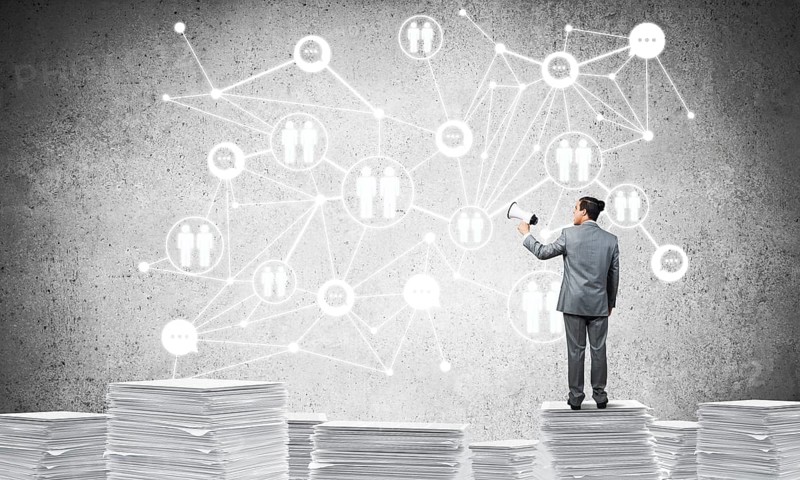 Businessman with speaker in hand standing on pile of documents with social network structure on background. Mixed media