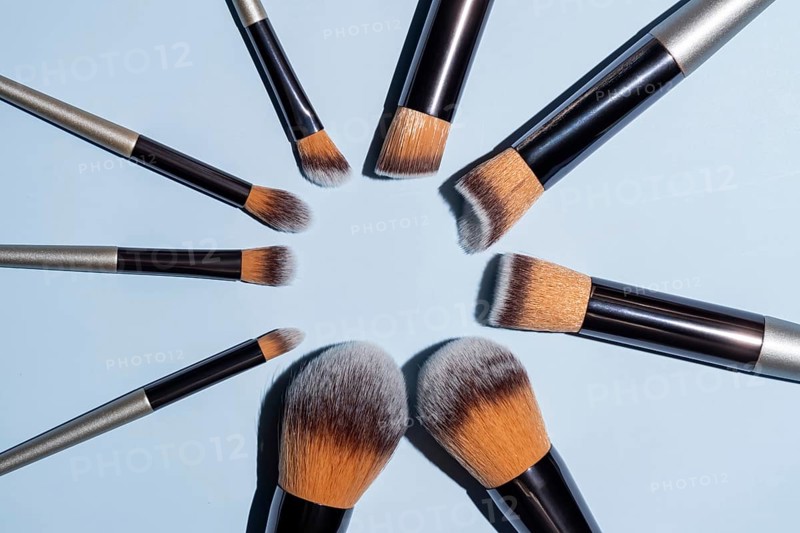 Make up brush sets arranged in a circle on blue background, top view with copy space. Cosmetics products
